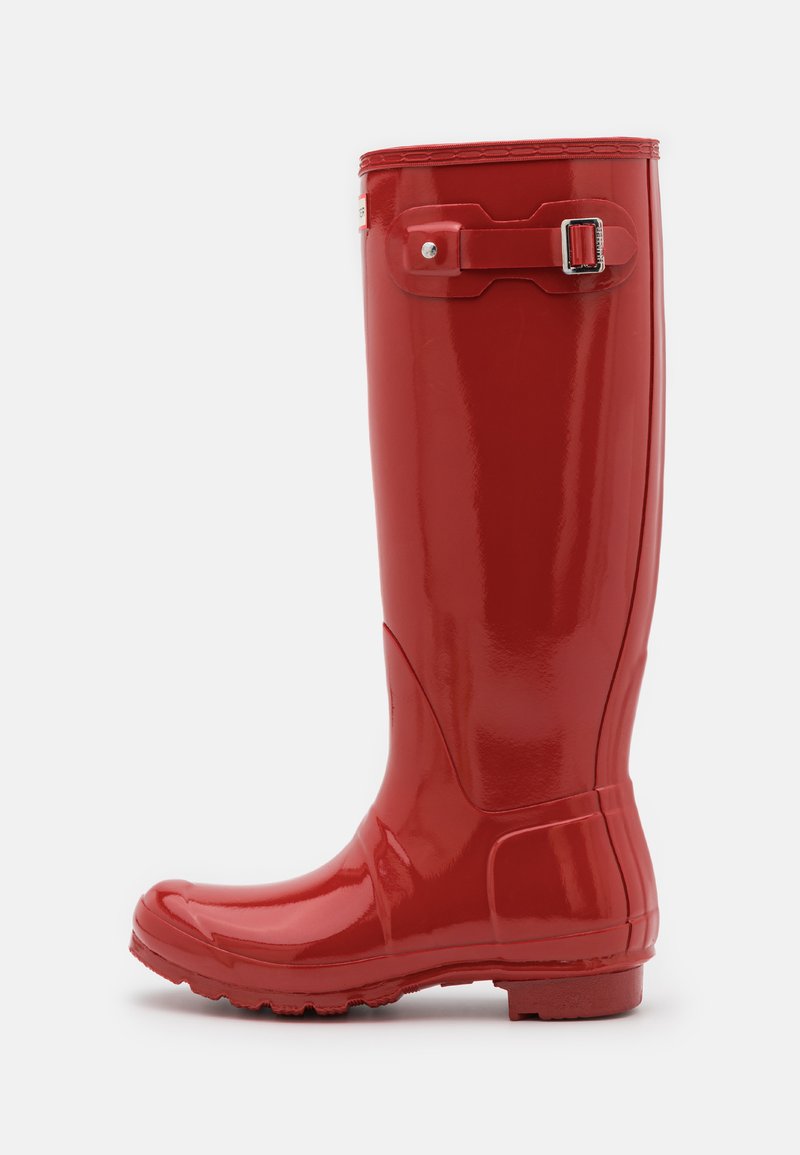 Rode rubberen regenlaars met hoge schacht, gladde glanzende oppervlakte, ronde neus, tekstuurzool voor grip en verstelbare gesp bovenaan.