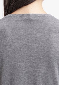Šedý pletený svetr s kulatým výstřihem, který má hladkou texturu a žebrované okraje kolem límce, představuje jednoduchý, neformální design.