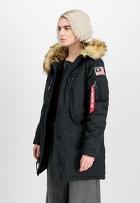Črna parka jakna s kapuco podloženo s umetnim krznom, zadrgo in gumbnimi zapirali, več žepi in z ameriško zastavo na rokavu.