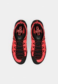 Pantofi sport roșii și negri, cu un plasă superioară, talpă texturată și șireturi negre. Talpa interioară prezintă grafică colorată și icoane clare.