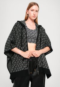 Black and gray knit poncho with an all-over logo pattern, featuring a zip front and a hood. Textured fabric with relaxed fit and short sleeves.