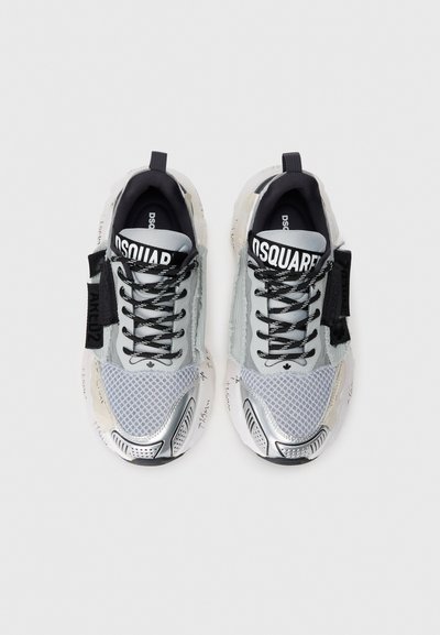 Adidași gri din plasă și piele cu accente metalice, șireturi negre, branding proeminent și detalii cu text scris de mână de-a lungul tălpii.