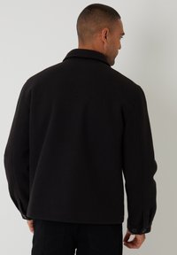 Sort jakke lavet af et struktureret stof, med en klassisk krave og knapmanchetter, designet til en afslappet pasform med let sænkede skuldre.