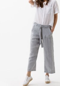 Světle šedé lněné kalhoty s páskem na zavázání, bočními kapsami a volným střihem, doplněné bílými plátěnými botami a volnou bílou košilí.