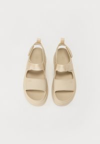 Beige sandaler med åpen tå-design, laget av glatt syntetisk materiale. Har en borrelåsrem, teksturert såle og logo-detalj.