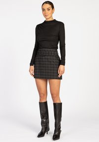 Zwarte lange mouwen top met een subtiele glans, gecombineerd met een geruite mini rok met een riem. Kniehoge zwarte leren laarzen maken de look compleet.