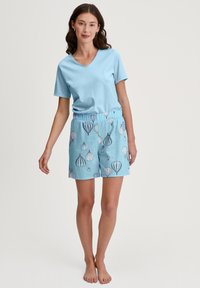 Lichtblauwe katoenen t-shirt met een v-hals, gecombineerd met blauwe shorts met een patroon van luchtballonnen in wit en marineblauw.