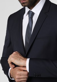 Navy suit with a notched lapel, white dress shirt, and a textured dark tie. Features four black buttons on the cuff and smooth fabric.
