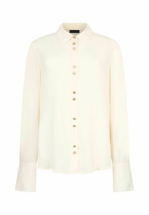 Blouse crème à manches longues avec col pointu et boutons décoratifs sur le devant ainsi que sur des poignets extra-larges.