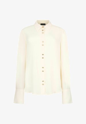 Blouse crème à manches longues avec col pointu et boutons décoratifs sur le devant ainsi que sur des poignets extra-larges.