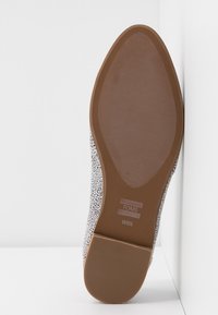 Semelle d'une chaussure TOMS pour femmes avec une semelle en caoutchouc marron, taille W6½, et une tige tachetée noir et blanc visible sur les côtés.