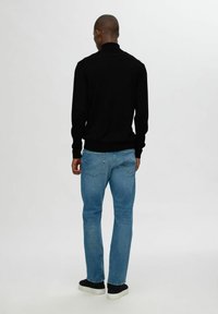 Svart stickad tröja med hög krage, parat med ljusblå raka jeans och svarta sneakers. Slät struktur och figursydd design.