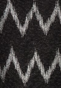 Svart textil med ett upprepande vitt zigzag-mönster som har en vertikalt randig textur på zigzag-linjerna.