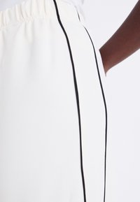 Pantalons blancs avec une bande latérale noire, dotés d'une taille élastique. Texture de tissu lisse, vue en gros plan mettant en évidence les détails du design.