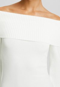 Vit off-shoulder tröja med ribbad halsringning och slät kropp. Har långa ärmar och en figurnära siluett.