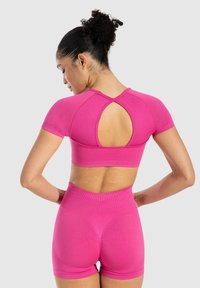 Set di abbigliamento attivo rosa composto da una maglietta a maniche corte con un taglio sulla schiena e pantaloni corti a vita alta, realizzato in un tessuto liscio e elastico.