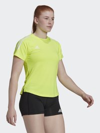 Camiseta atlética amarilla neón de mangas cortas, con el logo de Adidas en el pecho, combinada con pantalones cortos negros. Tejido texturizado con un diseño ajustado.