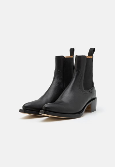 Botine din piele neagră până la glezna, cu panouri elastice pe laterale, vârf ascuțit și toc îngrămădit. Detaliu de cusătură distinctiv pe margini.