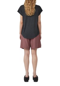 Donkergrijze top met korte mouwen en een ronde onderrand, gecombineerd met loszittende, stoffige rozenkleurige shorts. Zwarte platform schoenen maken de outfit compleet.