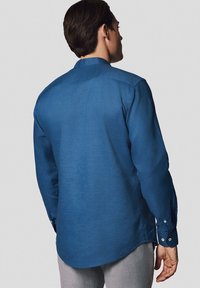 Niebieska koszula z długim rękawem, wykonana z teksturowanej tkaniny, z okrągłym kołnierzykiem i zapinanymi mankietami, z zaokrąglonym dołem i yoke z tyłu.