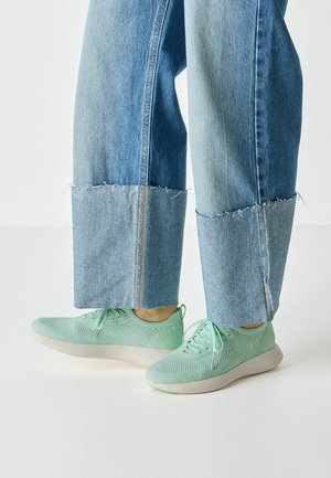 Hellgrüne gestrickte Sneakers mit strukturierter Oberfläche, rundem Schnürsenkel und glatter weißer Sohle. Getragen mit ausgefransten Jeans.