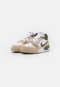 Pair of white and beige Nike sneakers with green accents, lace-up and a velcro strap, shown on a white background.