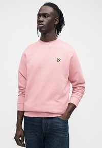 Sweatshirt cor-de-rosa com decote redondo, punhos e bainha canelados. Apresenta um pequeno logótipo bordado a amarelo e preto no peito.