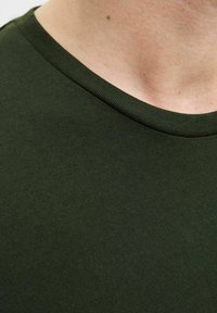 Dunkelgrünes Baumwoll-T-Shirt mit einem gerippten Rundhalsausschnitt und strukturiertem Stoff. Nahaufnahme, die die Detailstruktur des Stoffes und die Form des Ausschnitts zeigt.