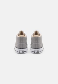 Szare tenisówki z płótna typu high-top z beżowym wnętrzem, czarnymi paskami i gumową podeszwą. Na pięcie znajduje się logo "CONVERSE ALL STAR".