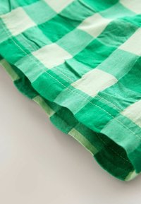 Zielono-biała tkanina w kratkę z widocznymi szwami na zakrzywionym łączeniu, na jasnym tle.