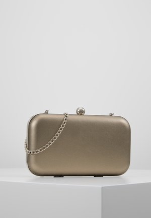 Prostokątna kopertówka z metalicznym brązowym wykończeniem, z zaokrąglonymi krawędziami, kulistym zapięciem na górze oraz łańcuszkiem na ramię, ustawiona na białym cokole.