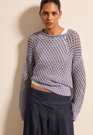 Light purple knitted sweater with a loose, open mesh design and ribbed cuffs, paired with a dark denim skirt featuring pleats.