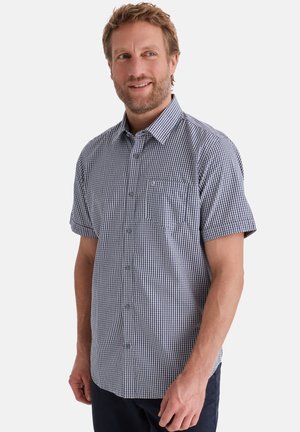 Mann trägt ein kurzärmeliges blau-weiß kariertes Hemd mit Knöpfen, lächelt, vor schlichtem weißem Hintergrund.