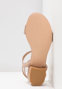 Sandale nude à lanières avec une tige lisse, un orteil arrondi et une semelle en caoutchouc texturée. Lanières fines et design minimaliste.