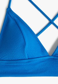 Blauwe textuur triangle bikini top met kruislings banden. Het materiaal lijkt rekbaar met een gladde afwerking. Details omvatten een gevoerde rand.