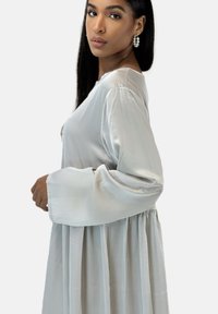 Robe légère gris clair en soie avec manches longues et taille froncée. Texture lisse et design fluide, avec un éclat subtil et un style minimaliste.