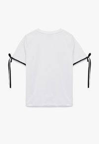 Witte T-shirt met een losse pasvorm, voorzien van zwarte lintstrikjes aan de mouwen en een ronde halslijn, gemaakt van zacht katoen.