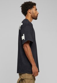 Musthave musta ülisuur t-särk pehmest tekstureeritud puuvillasegust. Omab valgeid abstraktseid mustreid mõlemal varral ning on lõdva voolu ja mahuga.