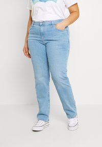 Jeans in denim blu chiaro con vestibilità dritta, caratterizzati da una vita alta, passanti per cintura e classico stile a cinque tasche. Abbinati a sneakers bianche.