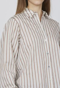 Stribet skjorte i lys beige med tynde brune lodrette striber, med spids krave og klare plastikknapper.