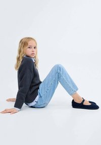 Woolen temno sivi pulover, svetlo modra srajca s ovratnikom, svetlo modri jeans in mornarsko modri platneni čevlji. Sedeč položaj na beli podlagi.