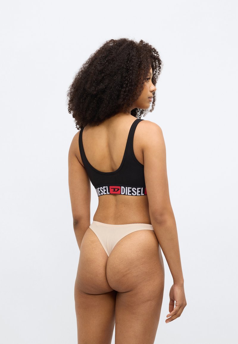 Black sports bra with a wide branded band featuring red and white text, paired with beige thong underwear, smooth fabric, simple design.
