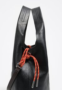 Czarna skórzana torba o fakturowanym wykończeniu, z górnym otwarciem zabezpieczonym czerwono-złotymi plecionymi sznurkami oraz eleganckimi, minimalistycznymi uchwytami.