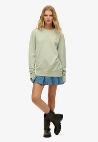 Sudadera verde menta con mangas largas, puños acanalados y ajuste relajado, combinada con una minifalda vaquera plisada y botines negros hasta el tobillo.