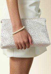 Sparkly white clutch covered in small, clear rhinestones, held in a hand with a pearl bracelet, featuring a sleek rectangular shape.