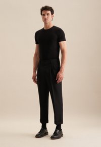 T-shirt noir ajusté associé à un pantalon noir taille haute, avec des plis sur le côté et des ourlets roulés, complété par des chaussures noires à lacets.