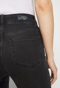 Černé džíny z denimu viditelné ze zadní strany, obsahující malou kapsu, jemné švy a štítek na pase.