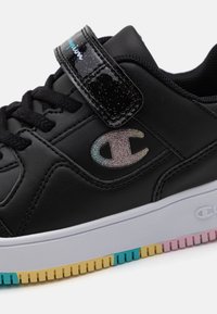 Black leather sneaker featuring a glossy black strap, rainbow-gradient logo, and a multicolored rubber sole.
