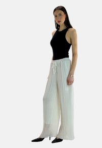White pleated wide-leg trousers with an elastic waistband, paired with a black sleeveless top, styled with black pointed heels.