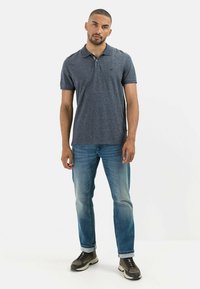 Granatowa koszulka polo z kołnierzykiem i dwoma guzikami, w połączeniu z jasnoniebieskimi dżinsami i ciemnymi sneakersami, charakteryzująca się teksturowanym materiałem.